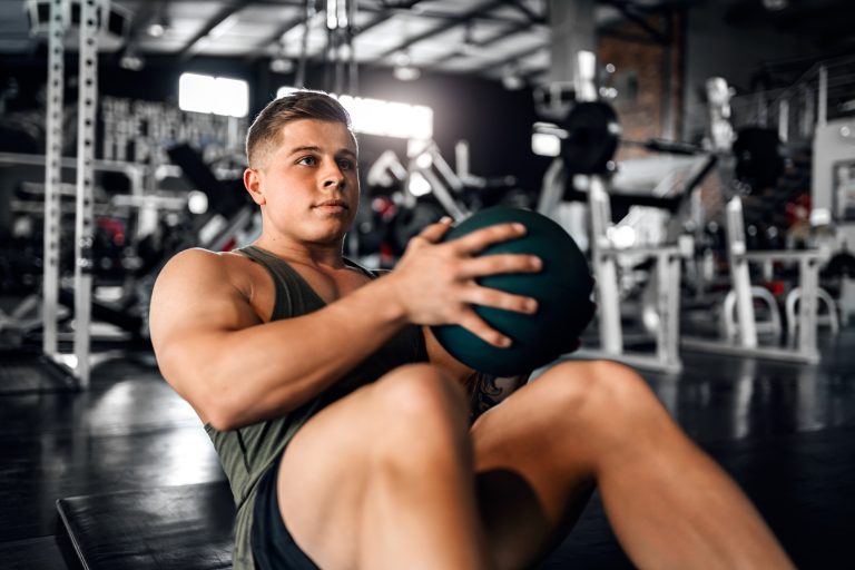 Young attractive muscular gen z athlete doing weighted ball abs exercises