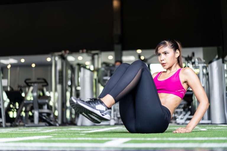 Young fit muscle Asian woman exercising and working out in gym. Pretty girl in sportswear sit up on the floor, looking in front of her focus on training building abs muscular, abdominal strength.